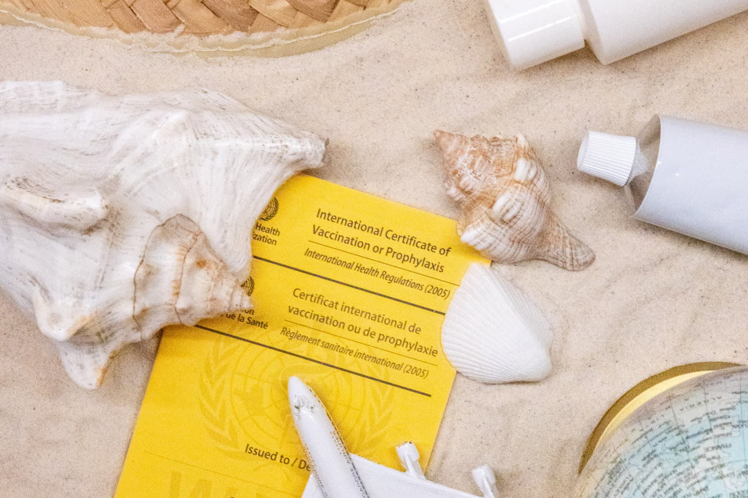 Impfbüchlein im Sand, umringt von Salbentuben und Muscheln